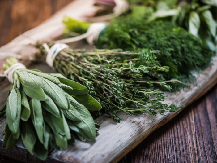 Fresh bundles of sage, thyme, and dill on a rustic wooden board, showcasing herbs for everyday cooking.